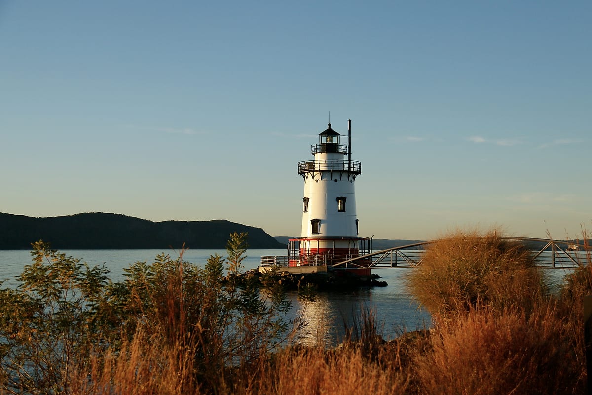 The white lighthouse in the river, orange shrubs on the shore in late light.